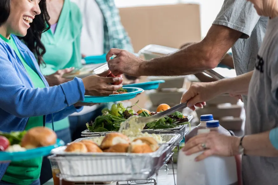 Volunteers serving salad, rolls and hot food from a buffet line